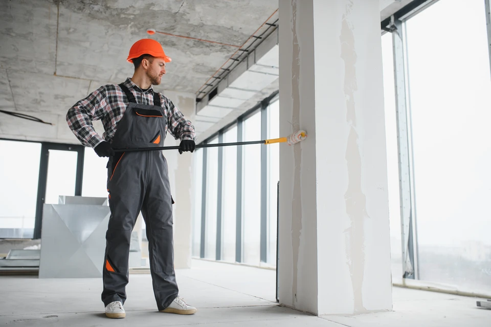 Peintre professionnel en tenue blanche appliquant de la peinture sur façade extérieure de maison résidentielle
