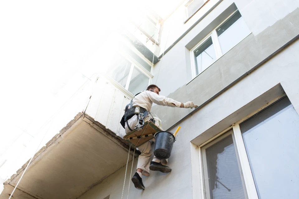 Homme effectuant des travaux de peinture extérieure sur mur crépi blanc avec rouleau à peinture à manche télescopique