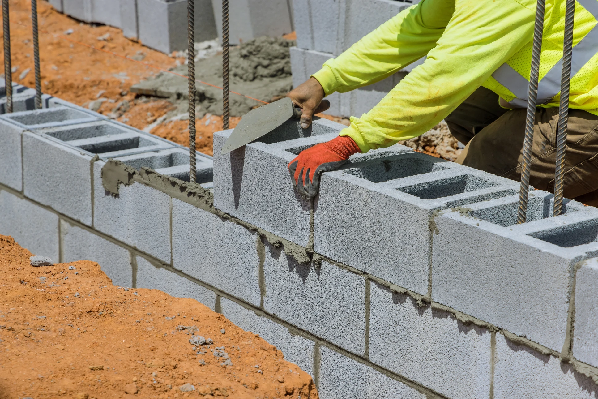 Scène extérieure de construction où un maçon applique du mortier sur un mur en parpaings à l'aide d'une truelle