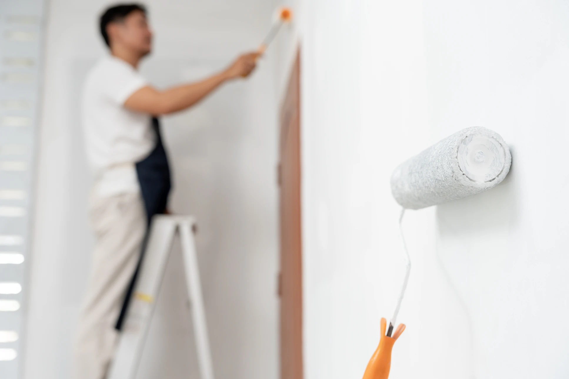 Peintre professionnel appliquant une peinture blanche sur un mur intérieur à l'aide d'un rouleau à peinture